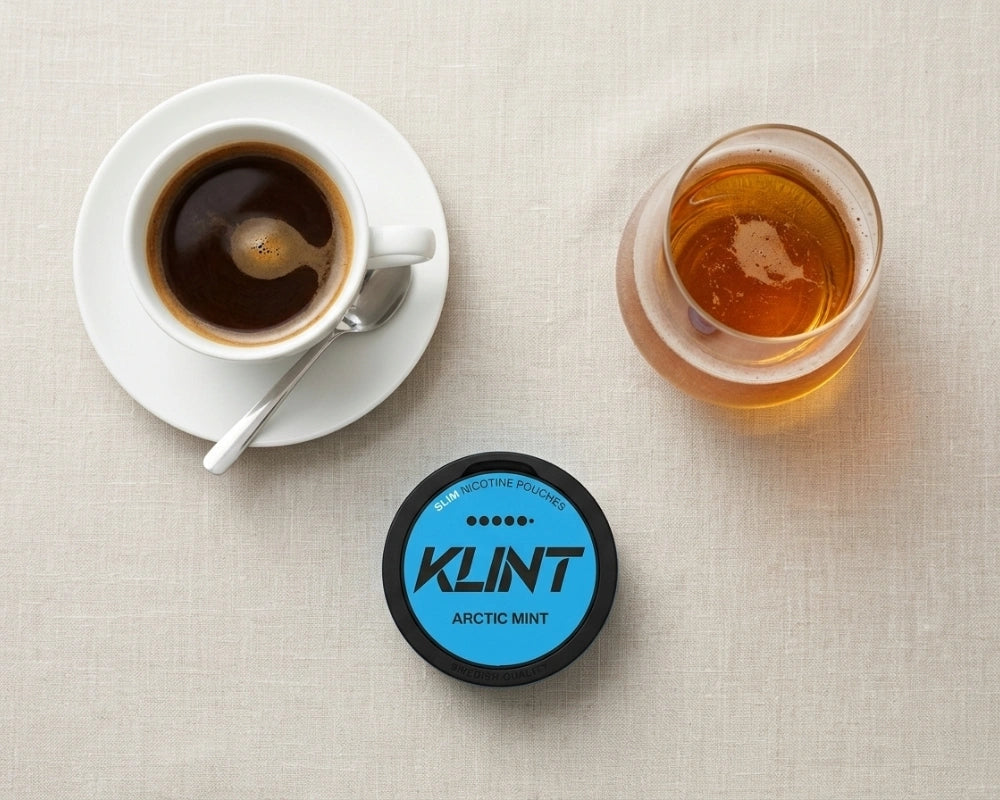 Cup of espresso, a glass of whisky and a KLINT Arctic Mist nicotine pouch can seen from above