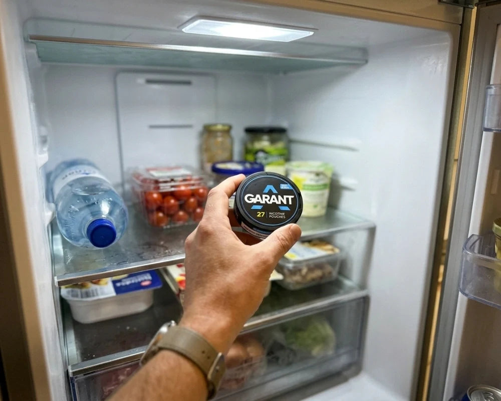 Hand placing a GARANT nicotine pouch can into an open fridge next to vegetables and bottles